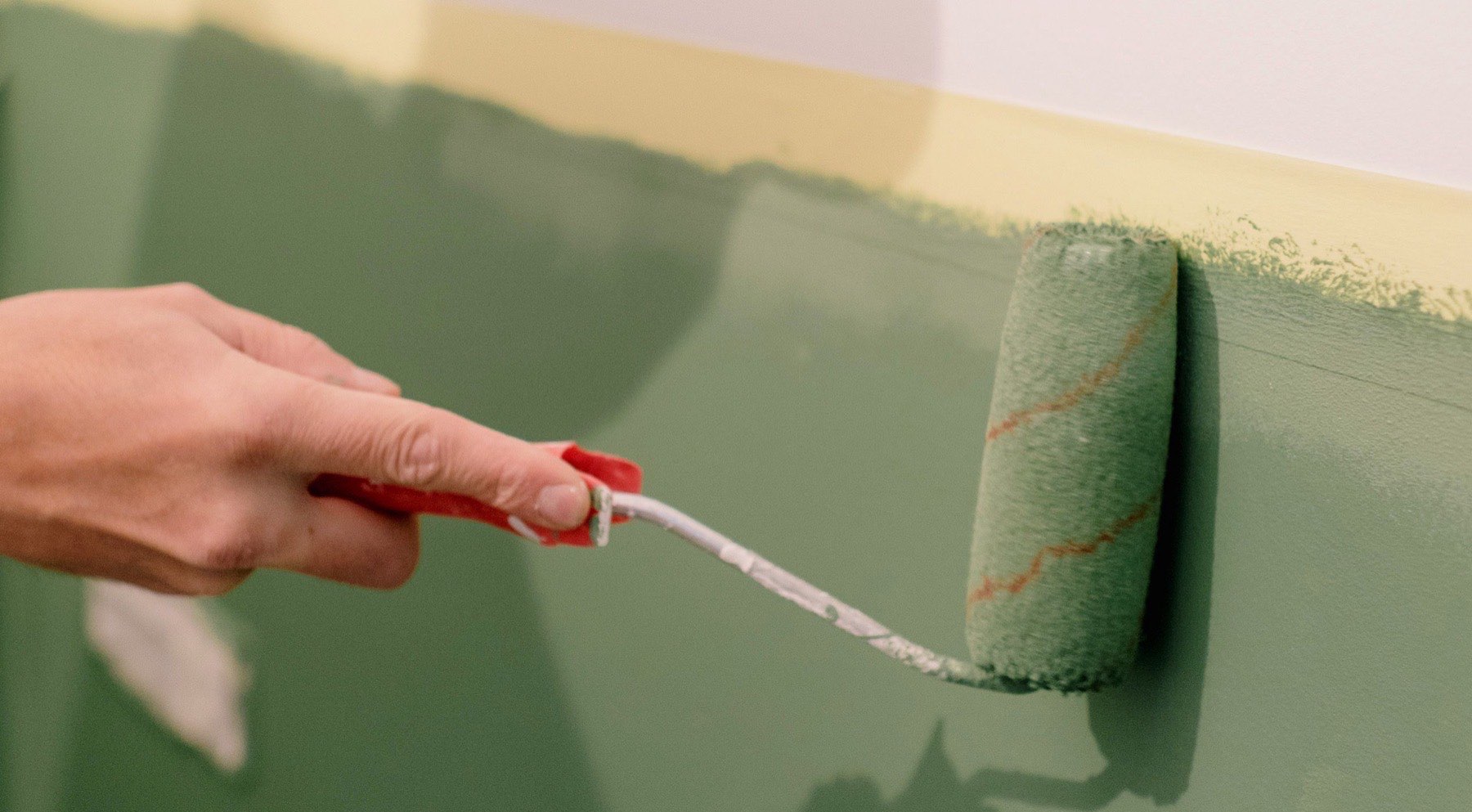Application d'une peinture verte au rouleau, geste d'un artisan peintre